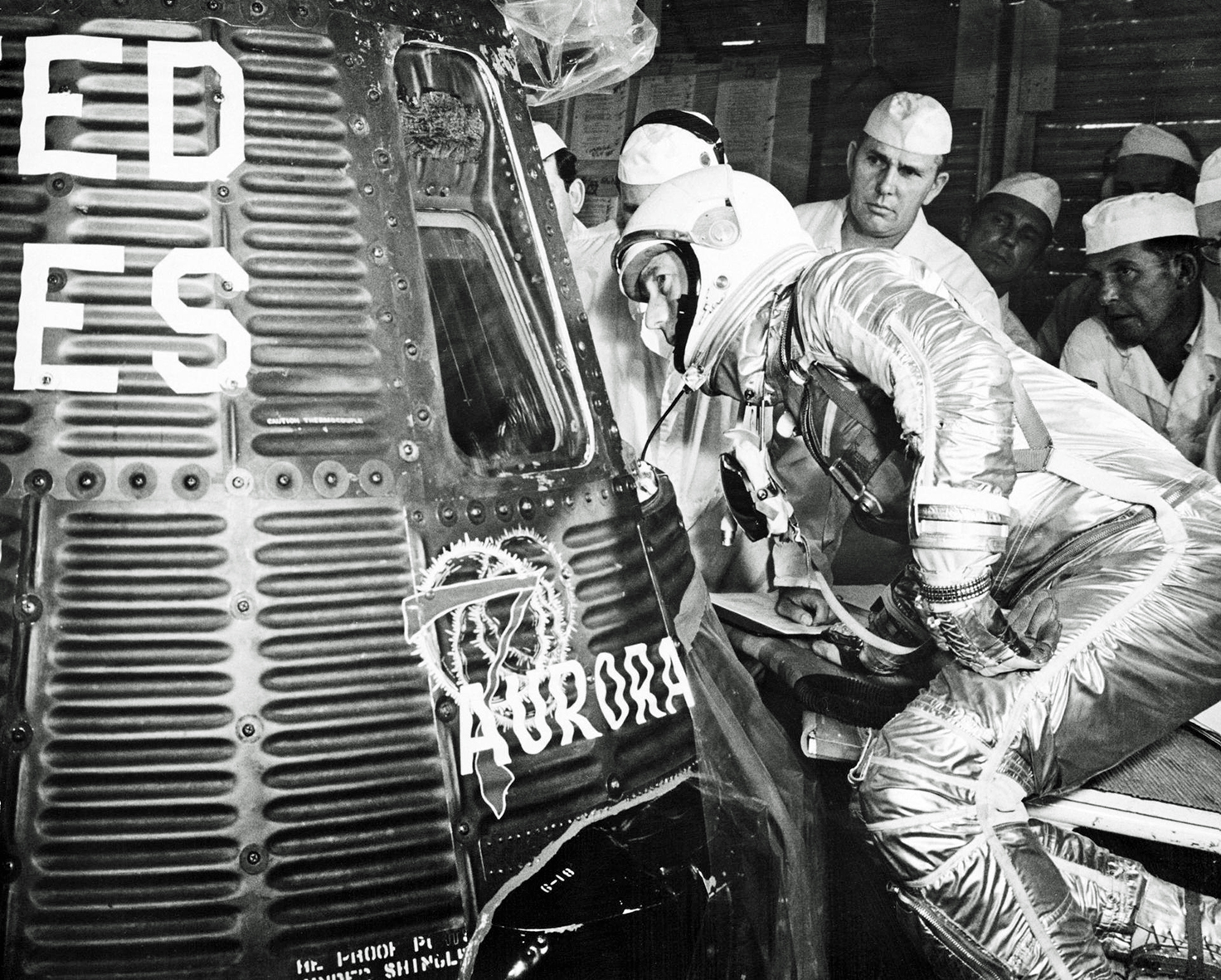 With technicians behind him, Carpenter looks through the window of his Aurora 7 capsule before being placed inside ready for launch.
