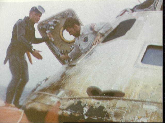 Schirra clambers out of the command module after splashdown, assisted by a navy diver