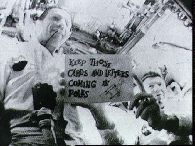 black and white tv transmission image of the crew holding up a cue card during one of the live broadcasts on Apollo 7