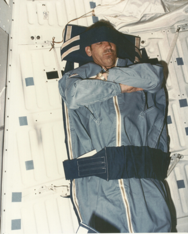 fabian sleeping aboard sts-7, his sleeping bag attached to the 'wall' with Velcro straps
