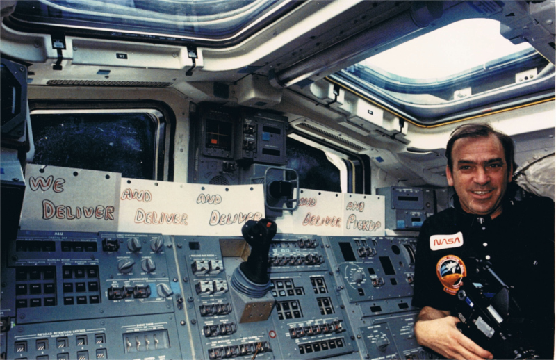 Fabian poses at the RMS station in front of hand-written signs marking the crew's successful retrieval and deployment of satellites.