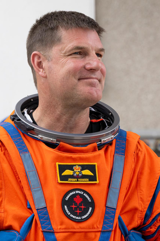 Portrait of a smiling Jeremy Hansen in orange flight suit on launch day for Artemis II