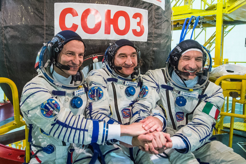 the three members of ISS Expedition 60 shake hands as they pose for photographs prior to their launch.