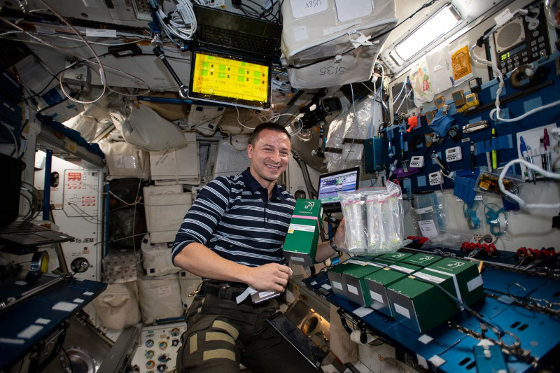 Morgan poses aboard ISS in front of a group of NanoRacks experiments in miniature laboratories.